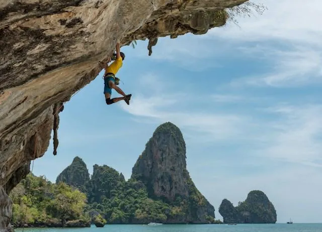 Un arrampicatore su una falesia di calcare a Railay, in Thailandia, con le formazioni carsiche e il mare delle Andamane sullo sfondo