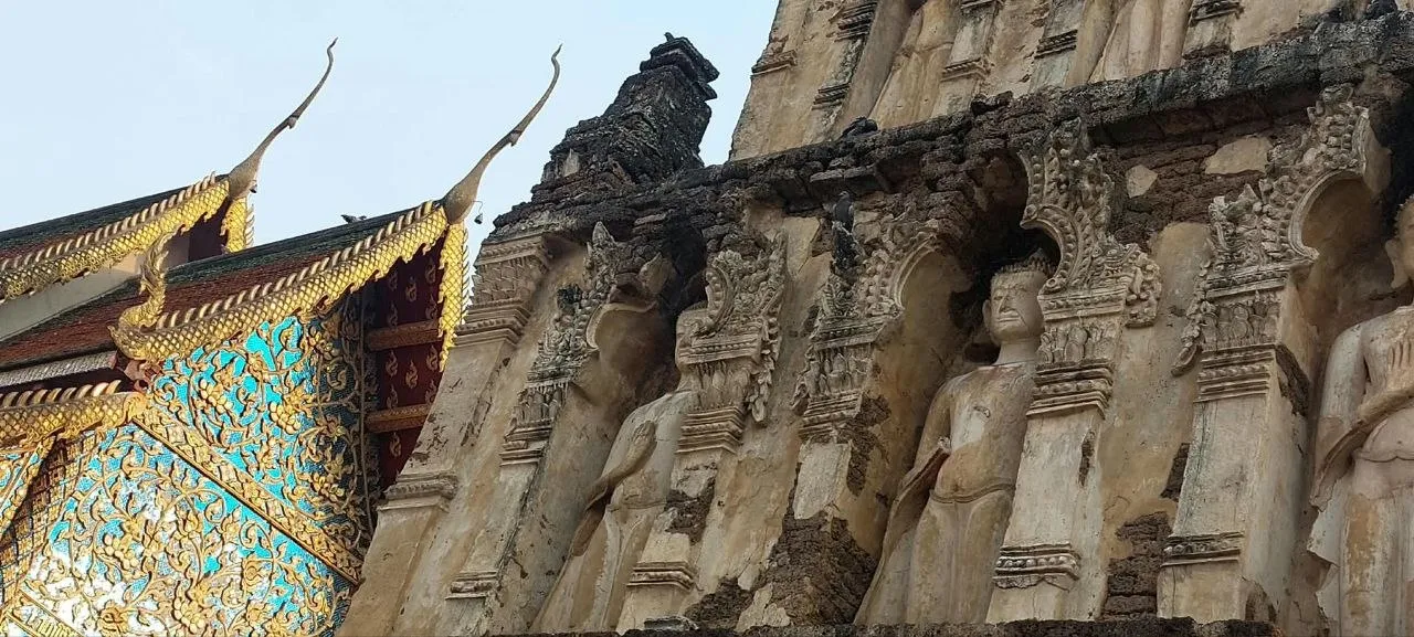 Wat Ku Kut (Wat Chamadevi) a Lamphun Le statue del Buddha nelle nicchie dell'antico stupa di Wat Ku Kut (Wat Chamadevi) a Lamphun, con il tetto dorato del viharn sullo sfondo