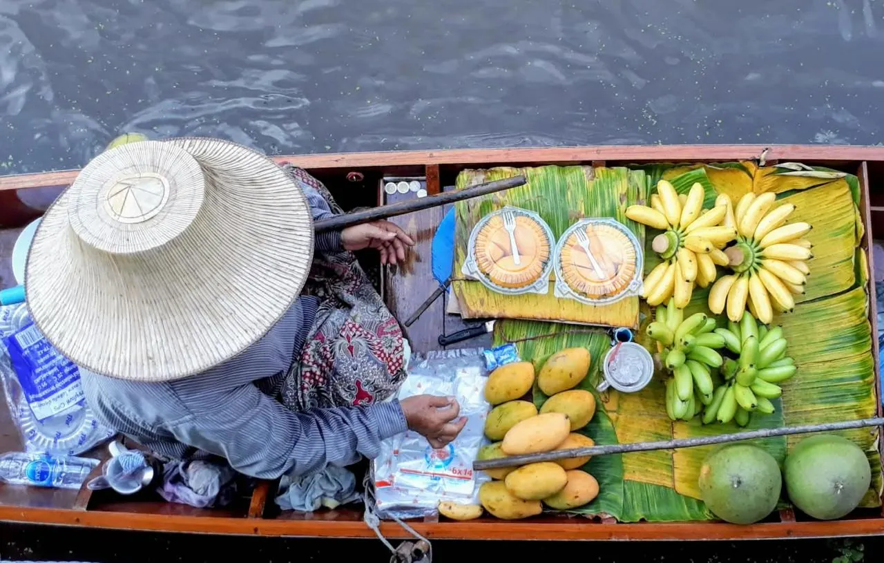 La frutta tropicale venduta direttamente dalle barche al mercato galleggiante Una venditrice di frutta sul suo canotto al mercato galleggiante, tra banane, mango e durian disposti sulle foglie di banano