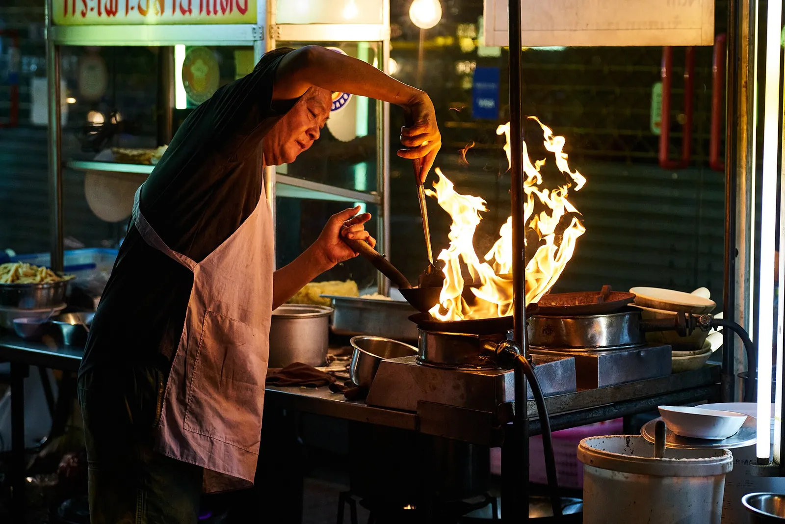 Cucina di street food a Bangkok con wok in fiamme e insegna in lingua thailandese